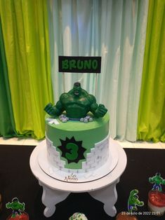 a green and white cake sitting on top of a table next to cupcakes