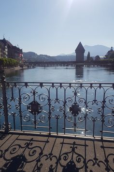 an iron railing overlooks the water and houses on either side, with mountains in the distance