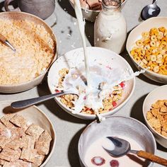 a table topped with bowls filled with cereal next to milk and other foodstuffs