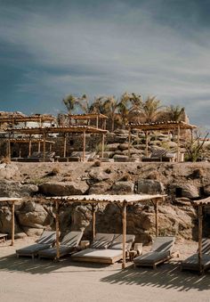 several lounge chairs sitting on top of a sandy beach next to palm trees and rocks