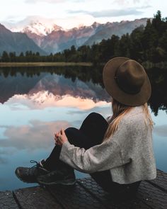 a woman sitting on a dock looking out at the mountains and lake in front of her