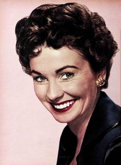 an old photo of a smiling woman with dark hair and green eyes, wearing a black jacket