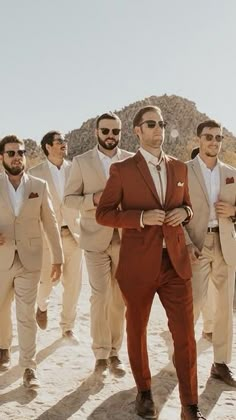 a group of men in suits and sunglasses walking across a desert area with mountains in the background