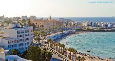 an aerial view of the beach and ocean with buildings in the background, including palm trees