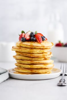 a stack of pancakes topped with fruit on top of a white plate next to a fork