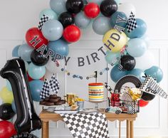 a birthday party with balloons, cake and race car decorations on a table in front of a happy birthday banner