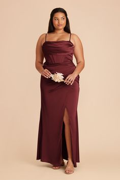 a woman in a long burgundy dress standing with her hands on her hips and looking at the camera