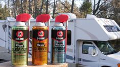 three spray cans sitting on top of a wooden table next to a camper trailer