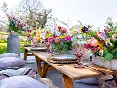 a wooden table topped with lots of vases filled with flowers next to pillows and blankets