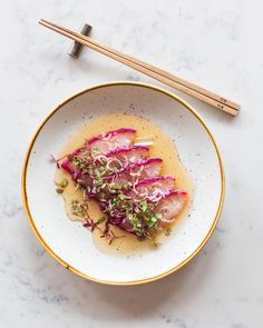 a white bowl filled with food next to chopsticks on top of a table