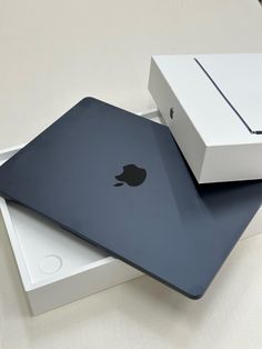 two apple laptops sitting on top of each other in front of a white box