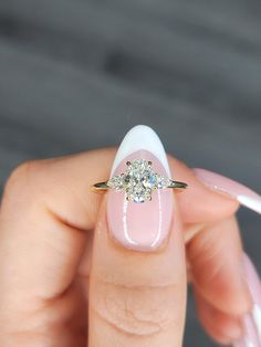 a woman's hand with pink and white nail polish holding a diamond ring