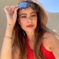 a woman in a red top and sunglasses posing for the camera with her hand on her head