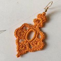 a pair of crocheted earrings hanging from hooks on a white surface with an orange thread