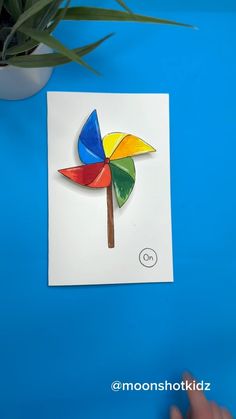 a hand is holding a piece of paper with a colorful pinwheel on it