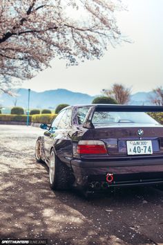 the back end of a bmw car parked in front of a tree with blossoming branches