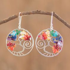 the earrings are decorated with multicolored beads and silver wire, hanging from a tree branch