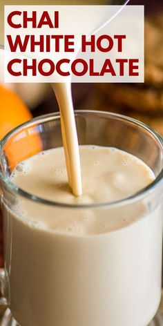 a glass filled with white hot chocolate sitting on top of a table next to an orange