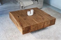 a wooden table with two white vases on it in front of a gray couch