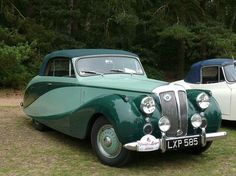 two old cars parked next to each other in the grass with trees in the background