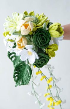 a bridal bouquet made with crocheted flowers and leaves is being held by someone's hand