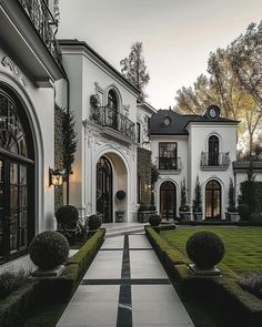 a large white house with lots of windows and bushes in front of it on a cloudy day