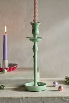 a green candle holder sitting on top of a table next to a pink and purple candle