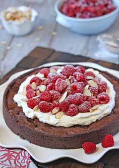 a chocolate cake topped with raspberries and almonds on a white platter