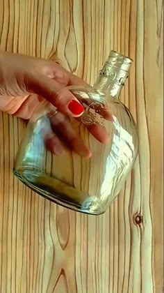 a woman's hand holding onto a glass bottle on top of a wooden table