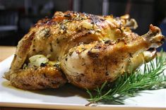 a whole chicken on a white plate with green garnish and rosemary sprigs