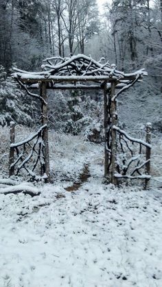 a wooden structure in the middle of a snow covered field with trees and bushes behind it