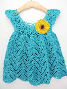 a crocheted blue dress with a yellow flower on the front and back, hanging from a wooden hanger