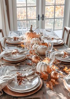 a table set for thanksgiving dinner with pumpkins and silverware