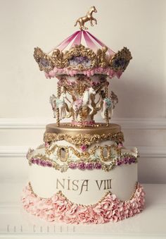 a three tiered carousel cake with pink flowers on the bottom and gold trimmings