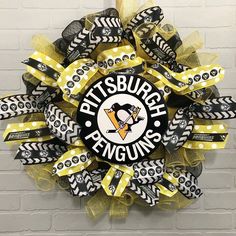 a pittsburgh penguins deco mesh wreath hanging on a brick wall with yellow and black ribbons