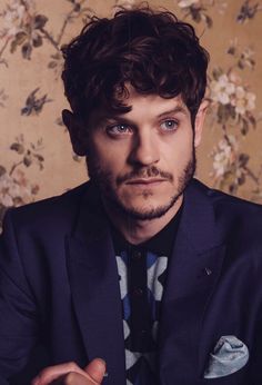 a man in a suit and tie sitting on a couch with his hands folded out