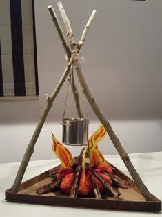 a fire pit made out of sticks and logs with a pot hanging from the top