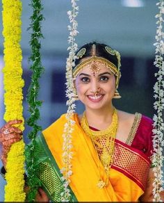 a woman in a yellow and red sari holding a pole with flowers on it