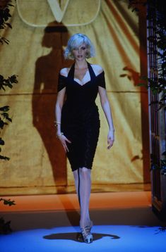 a woman walking down a runway in a black dress