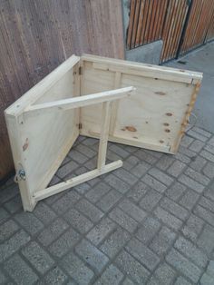 a wooden box sitting on the ground next to a fence and building with it's door open