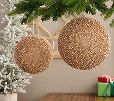 two ornaments hanging from the ceiling next to a christmas tree with presents under it on a wooden table