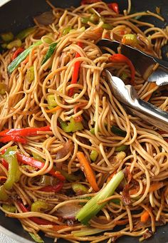 a stir fry with noodles and vegetables being stirred by tongs