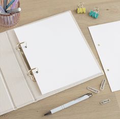 a binder, pen and paper clips on a wooden table with an empty notebook