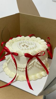 a white cake in a box with red ribbon around it and an open card board behind it