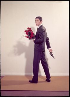 a man in a suit and tie holding a bouquet of flowers while standing next to a wall