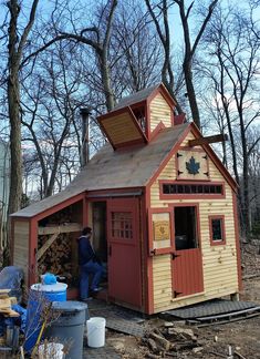 a small shed with a man standing next to it in the middle of some trees