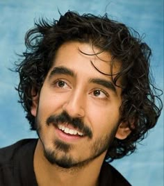 a man with curly hair and a beard smiles at the camera while wearing a black shirt