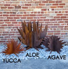 three metal sculptures sitting next to each other in front of a brick wall with the words yucca aloe agave on it