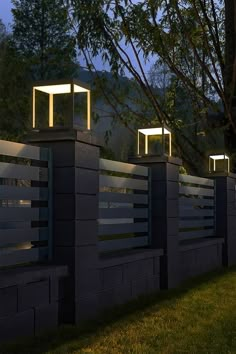 three lights are on the side of a fence in front of some trees and grass