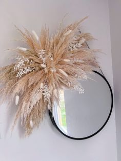 a mirror hanging on the wall with dried grass in front of it